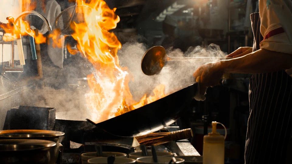 Flames rising from a wok in a restaurant kitchen